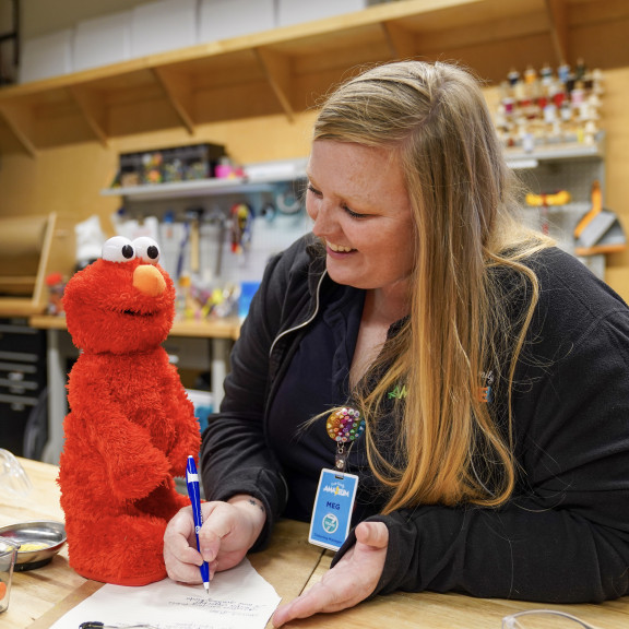 Amazeum Employee Writing Next To An Elmo Doll