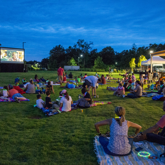 People Sitting On Blankets Watching A Movie Outside On Projector