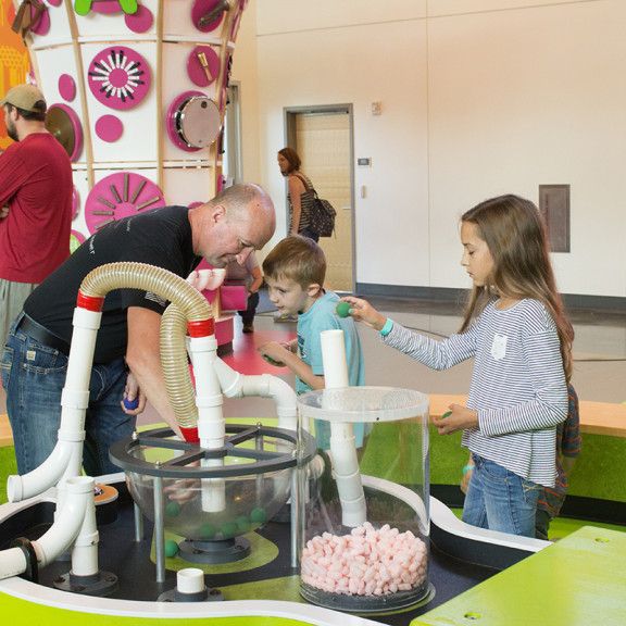 Family Playing With Foam Ball And Vacuum Tube Exhibit