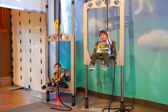 Two Boys In Chairs Pulled Up And Down By Giant Ropes And Pulleys